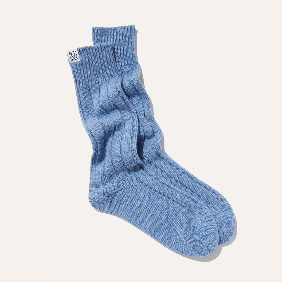 Margaux’s The Cozy Sock - Blue Cashmere is a ribbed, light blue crew sock made from a soft wool-cashmere blend, finished with a small white tag near the top and shown against a plain white background.