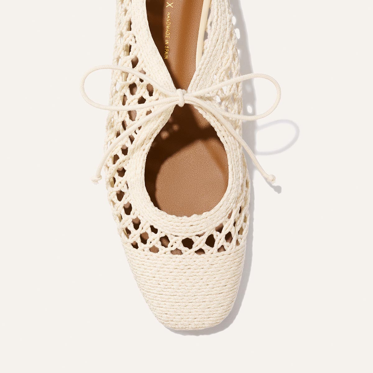 Top view of The Luna - Ecru Macrame by Margaux, a cream cotton macrame ballet flat with a front bow and tan insole, displayed on white—a chic summer essential.