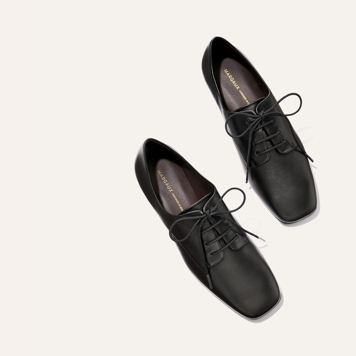A pair of Margaux's The Billie Derby in black nappa leather, featuring square toes and lace-up design, displayed on a light-colored background.