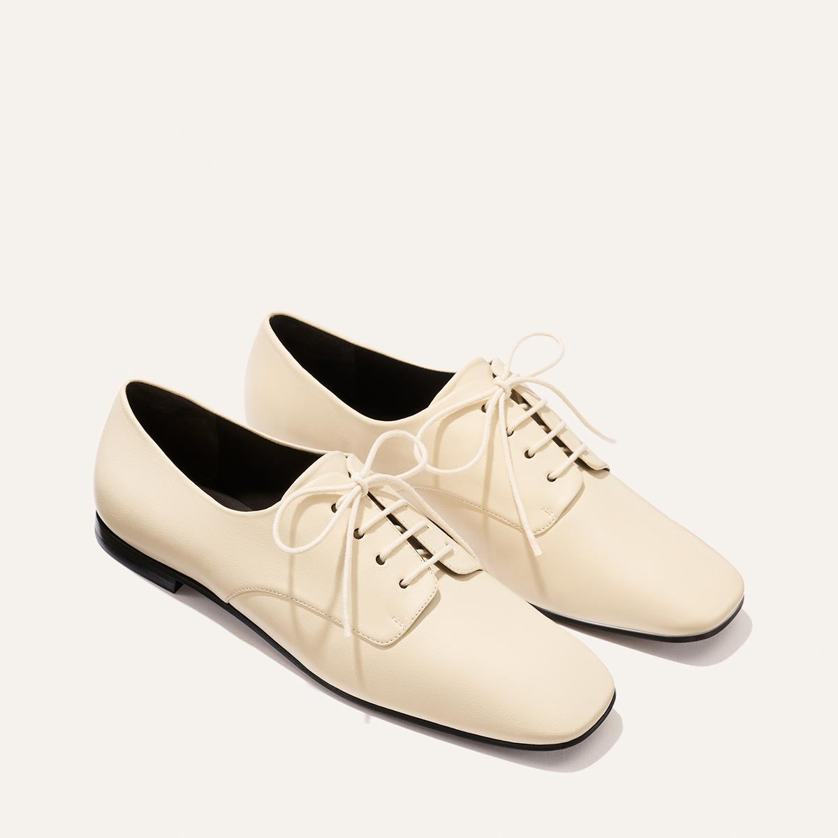 A pair of Margaux's The Billie Derby shoes in Vanilla Nappa—cream-colored, lace-up dress shoes with black soles—photographed on a plain white background.