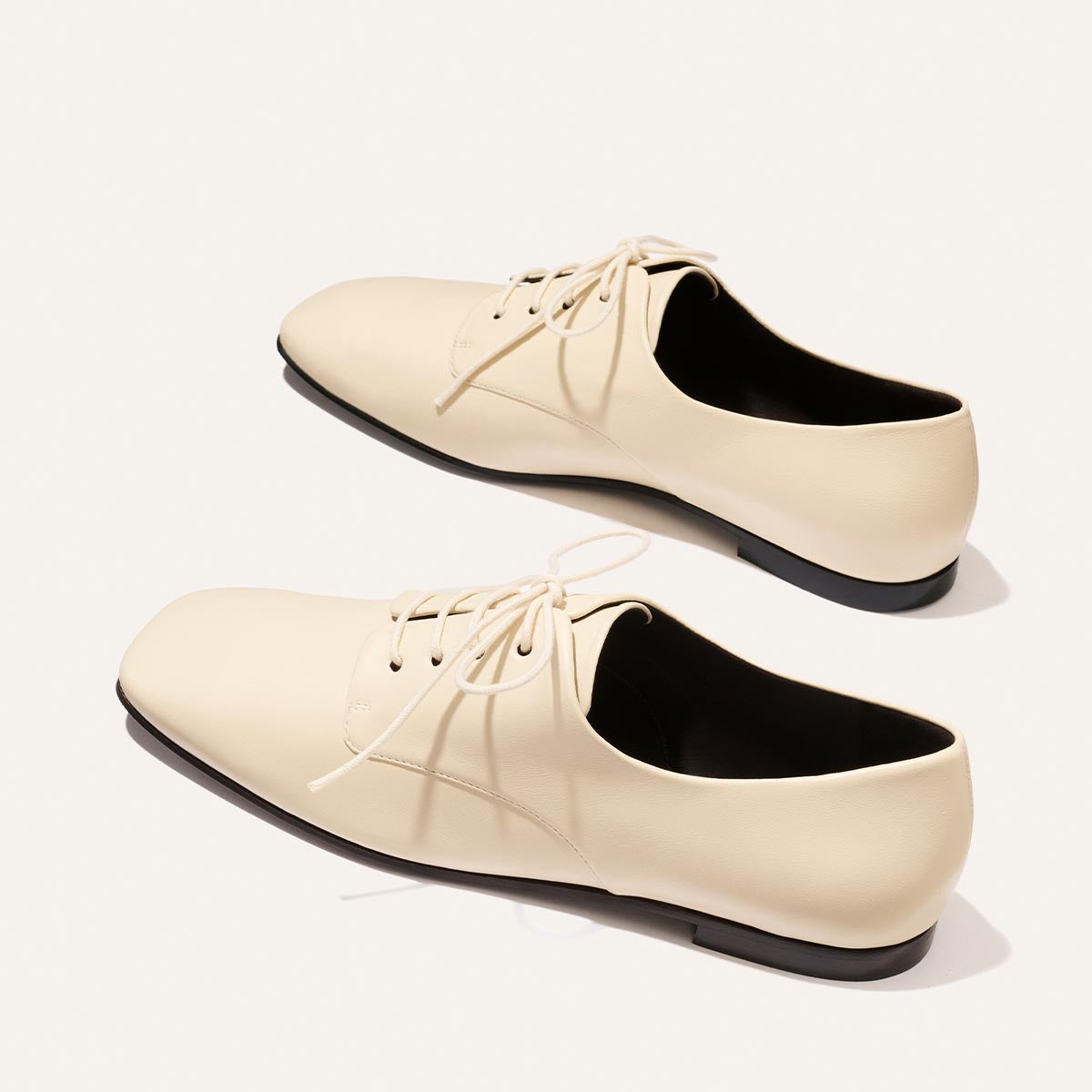 A pair of Margaux's The Billie Derby - Vanilla Nappa lace-up shoes with black soles, displayed on a white background.