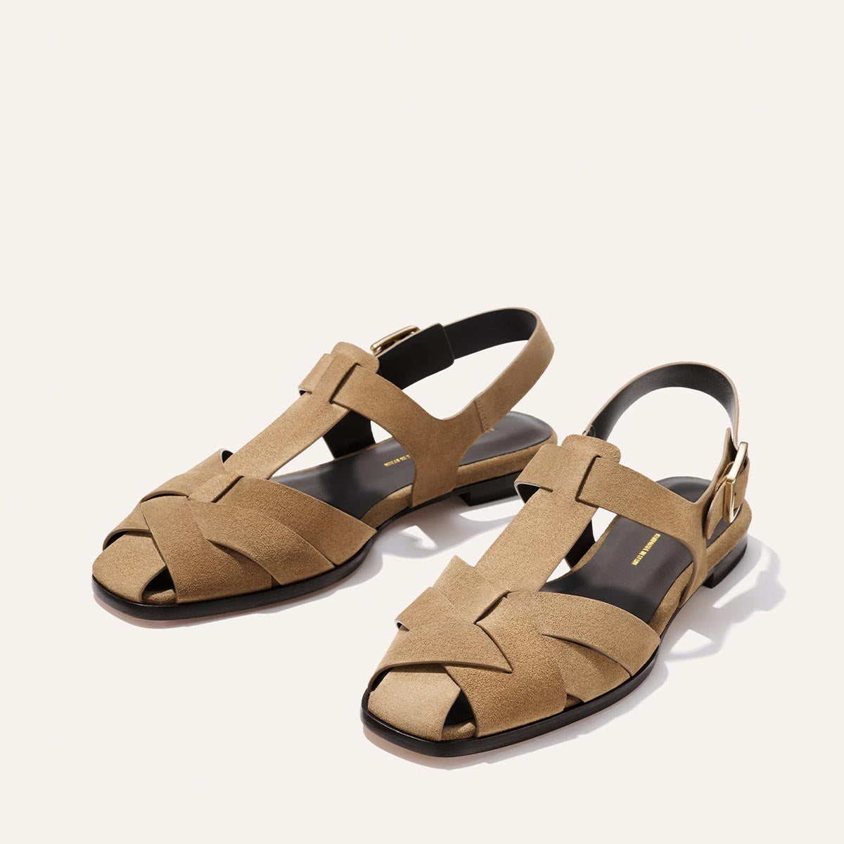 Pair of tan sandals with black soles on a white background