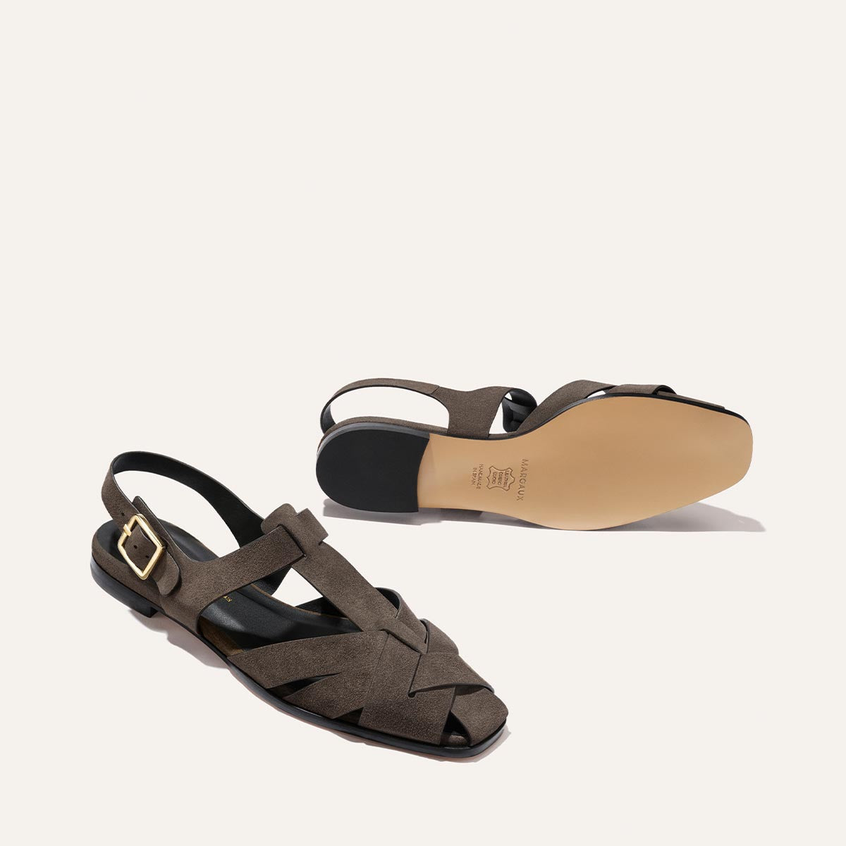 Margaux’s The Calypso Fisherman in English Brown Suede features modern interwoven crisscross straps, a sleek gold buckle, and a flat black sole—pair shown upright and sole side up for detail.