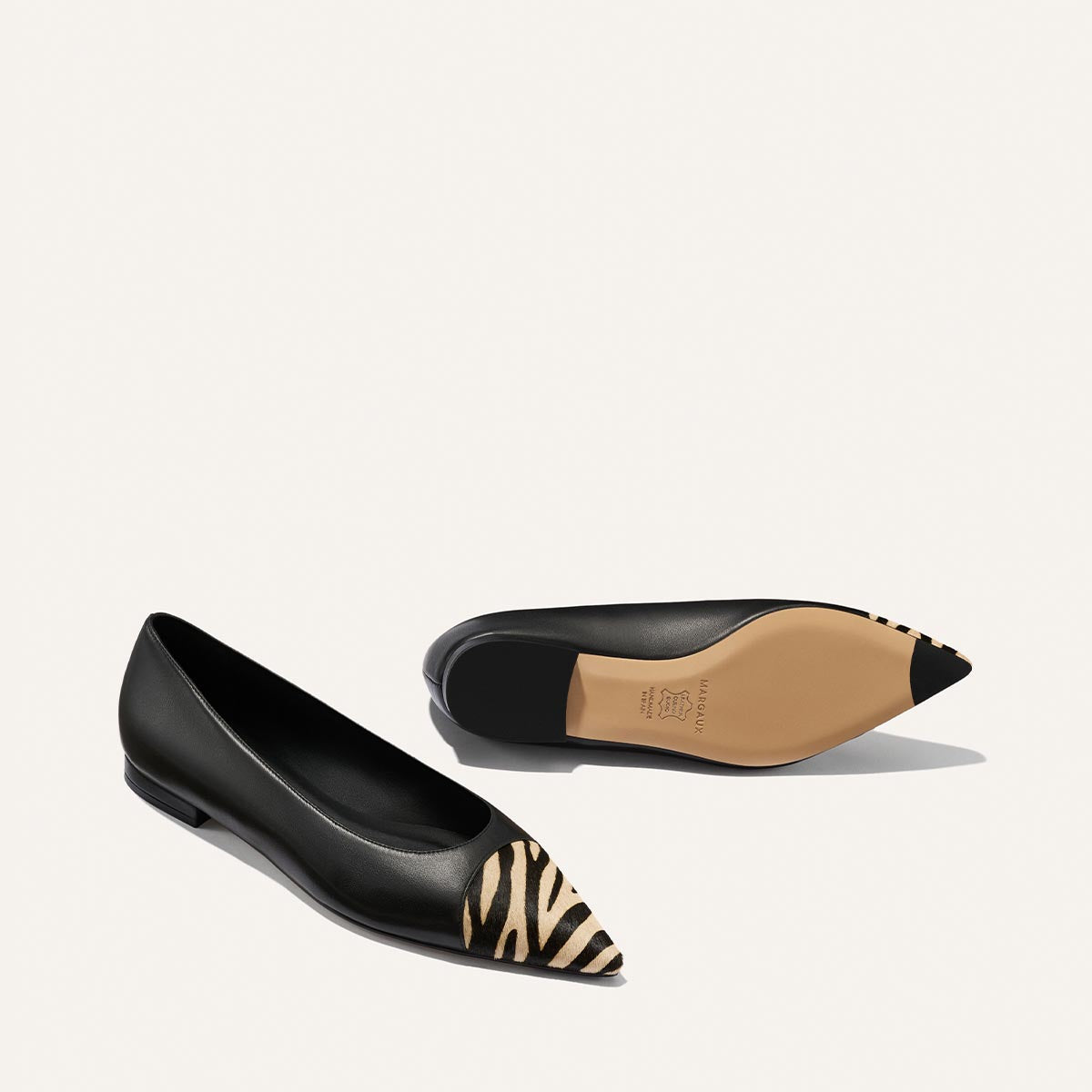 Introducing The Alba by Margaux: a pair of black nappa ballet flats featuring a pointed toe, accented with zebra haircalf detailing across the front and finished with a beige sole. Designed for comfort with a padded insole, these shoes are elegantly displayed against a plain white background.