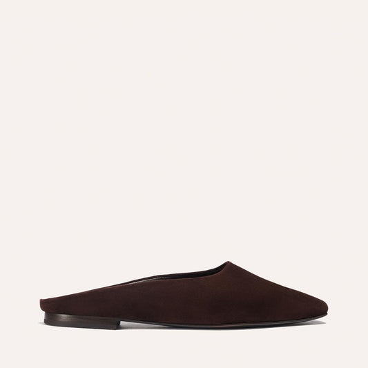 The Clara - Espresso Suede by Margaux is a minimalist dark brown slip-on mule with a slipper-like silhouette and flat sole, shown from the side on an off-white background.