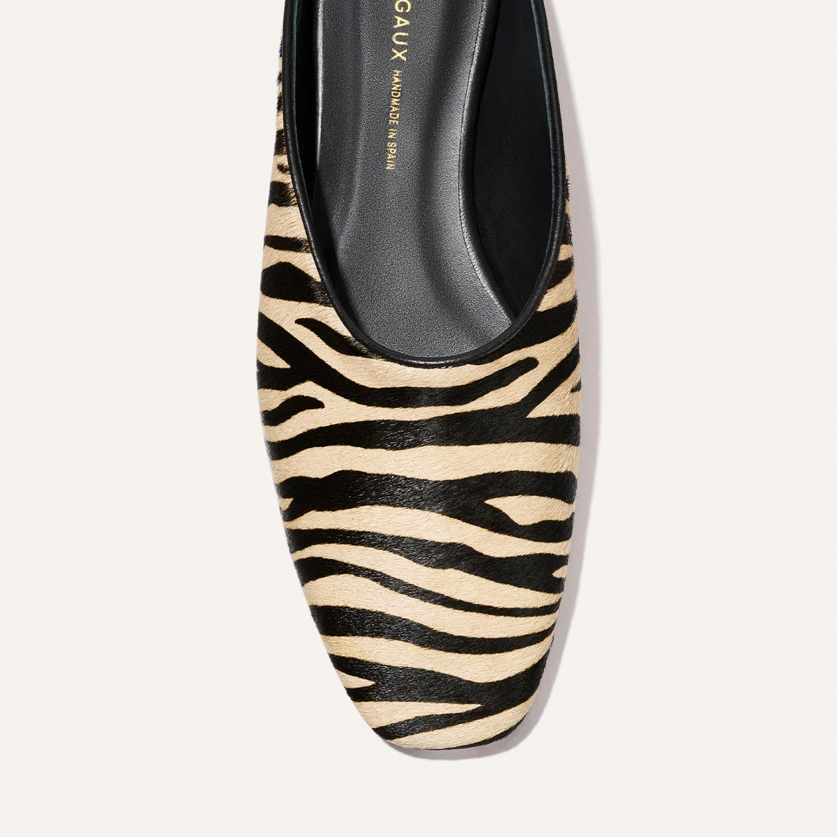 A close-up top view of The Clara - Tan Zebra Haircalf flat shoe by Margaux, featuring a black and beige zebra print pattern with a black interior.