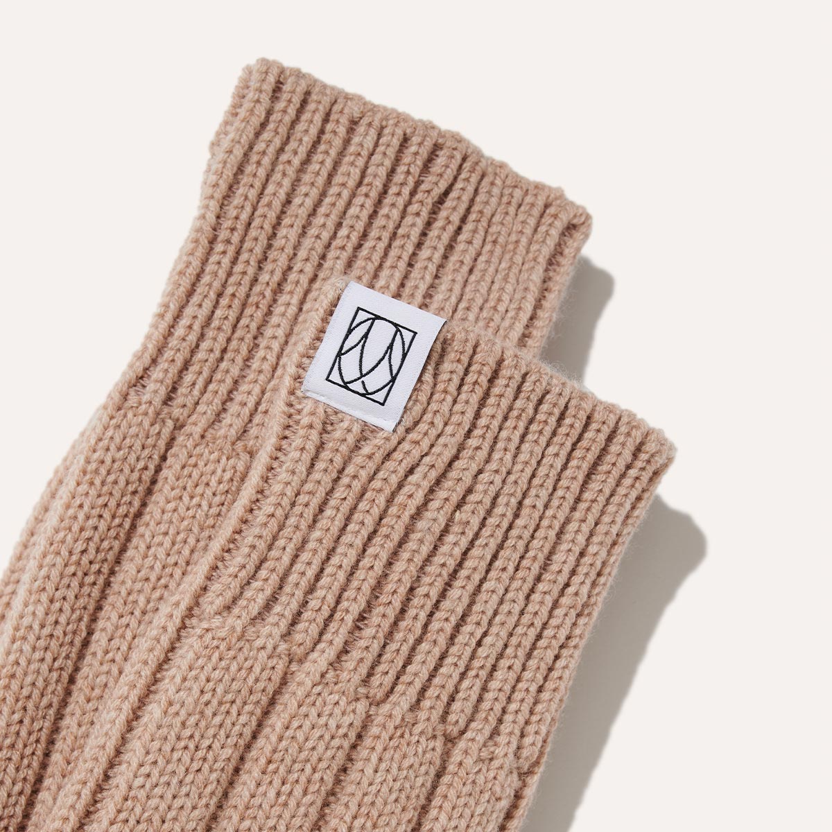The Cozy Sock - Oatmeal Cashmere by Margaux is crafted from a soft wool-cashmere blend, featuring a white patch with a black abstract logo, and shown on a plain white background.