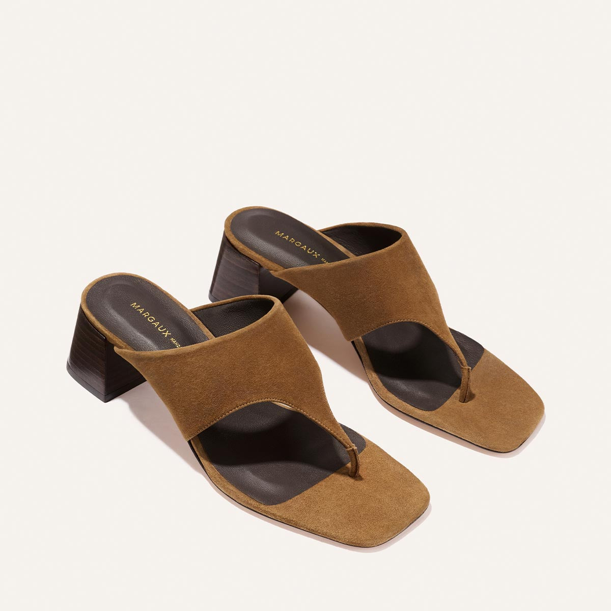 The Deia 50 - Nutmeg Suede by Margaux are brown suede heeled sandals with wide straps, a toe loop, square toe, and chunky mid-height wooden heels.