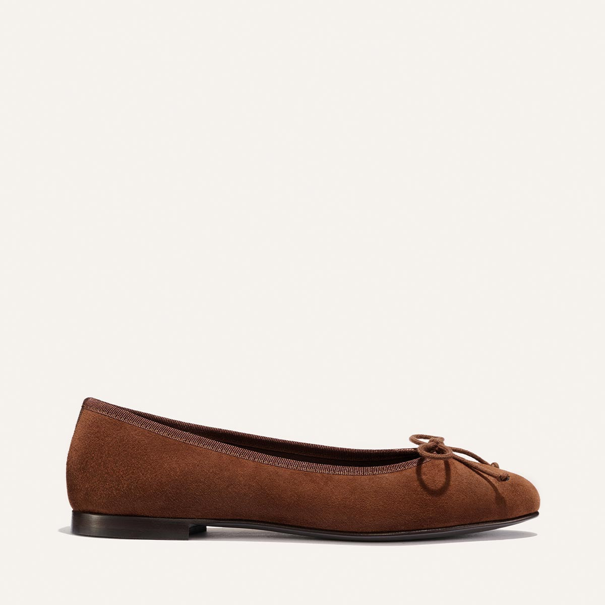 A side view of Margaux's The Demi in Ganache Suede—a brown, handmade-in-Spain ballet flat—featuring a petite bow on the toe, shown against a plain light background.