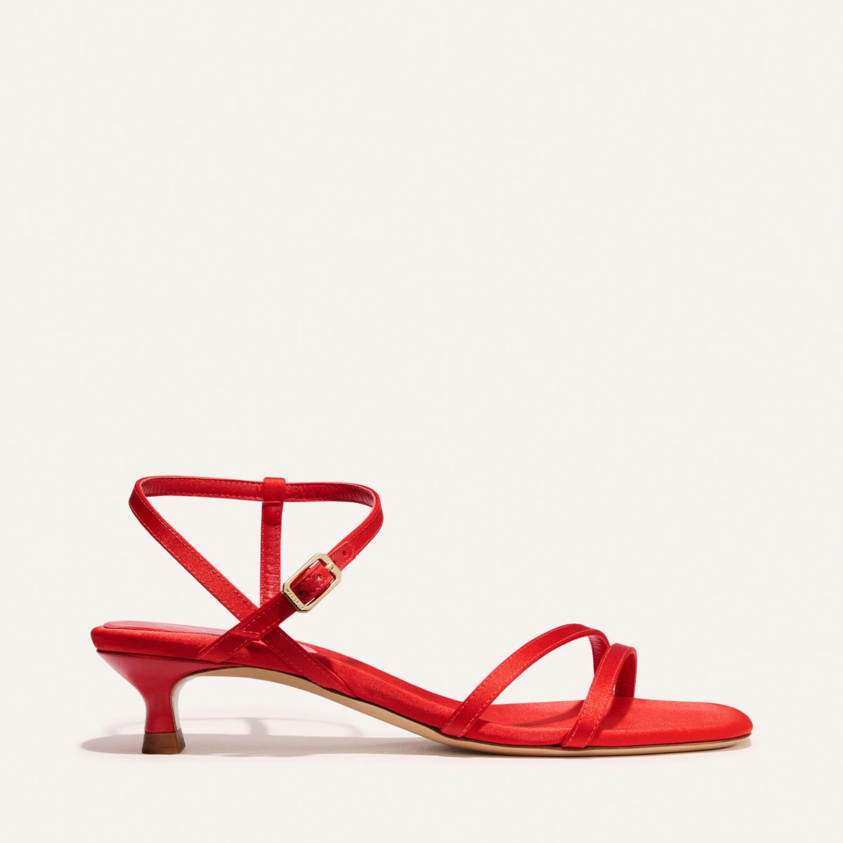The Dylan Sandal by Margaux in Poppy Satin features a low kitten heel, thin ankle strap with gold buckle, and two narrow toe straps, shown on a neutral background.
