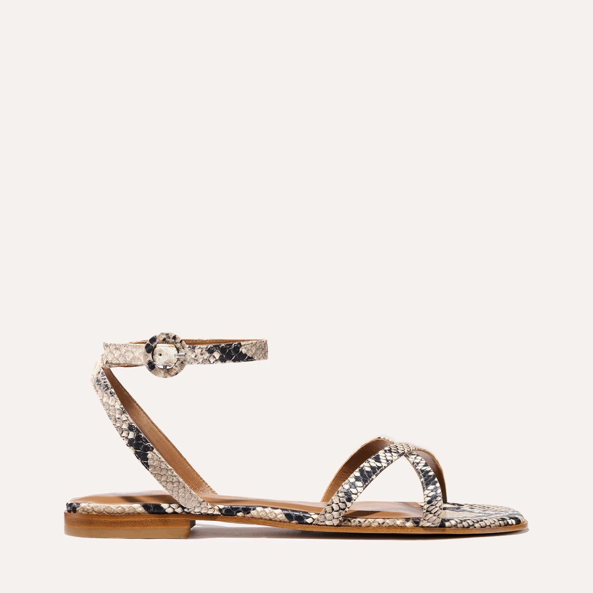 The Flat Sandal - Natural Python Embossed by Margaux features a barely-there design with a thin buckled ankle strap and two crisscrossing toe straps, showcasing timeless style in a subtle snakeskin pattern.