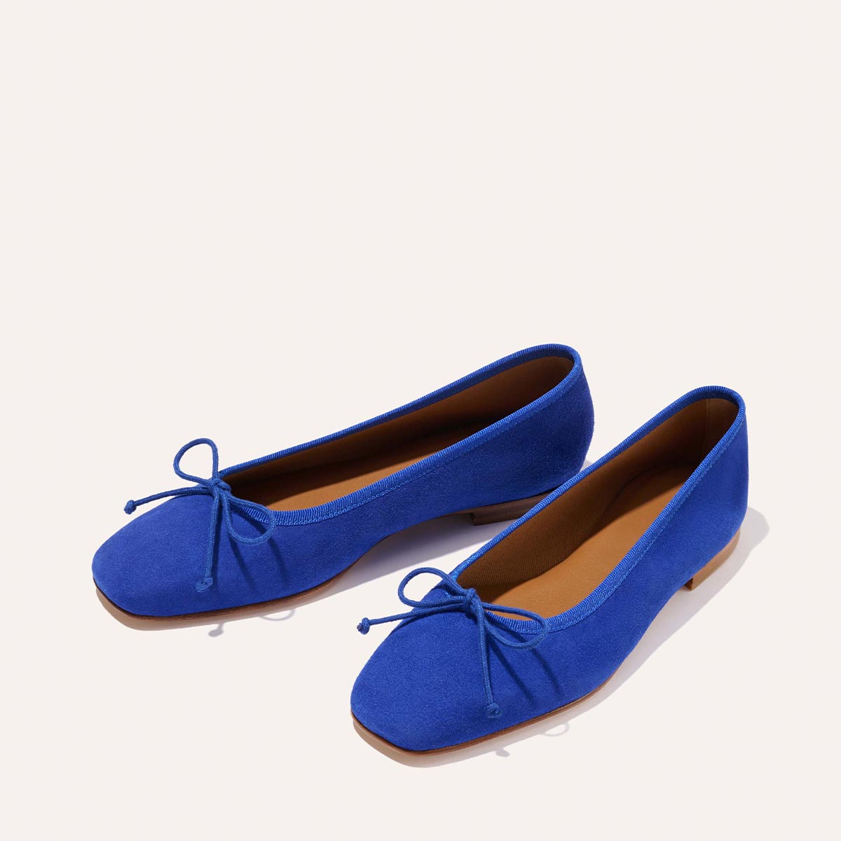 The Fonteyn - Cobalt Suede by Margaux: handcrafted bright blue ballet flats with front bows, tan insoles, and low heels, displayed on a light background.
