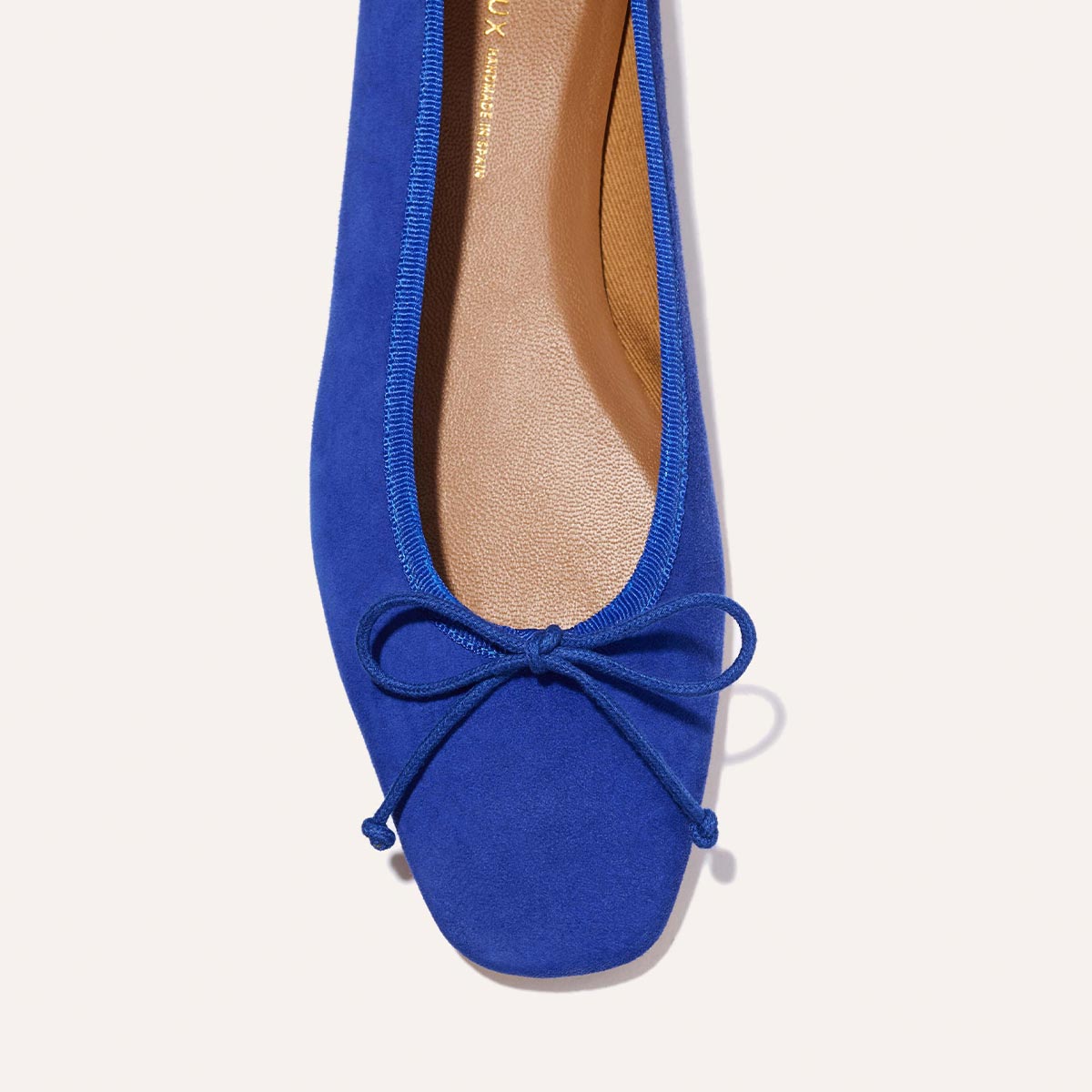 A close-up of Margaux's The Fonteyn - Cobalt Suede ballet flat, featuring vibrant blue suede, a rounded square toe, matching bow detail, and a tan insole with gold lettering.