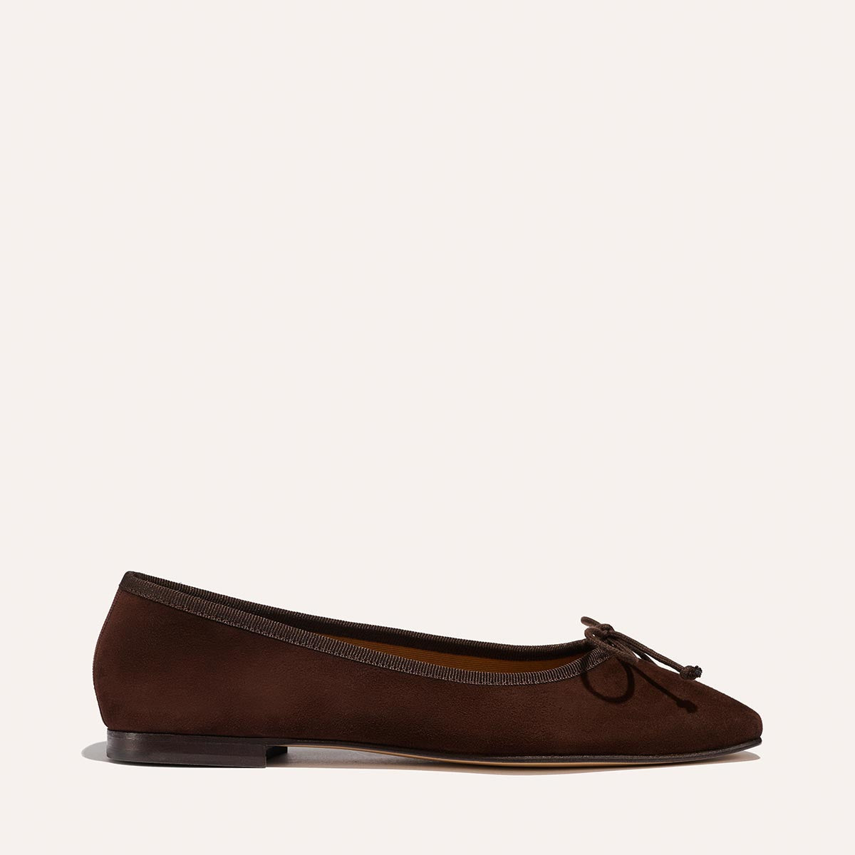 The Fonteyn - Espresso Suede by Margaux is a dark brown handcrafted ballet flat with a round toe, delicate front bow, and thin black sole, shown on a light background.