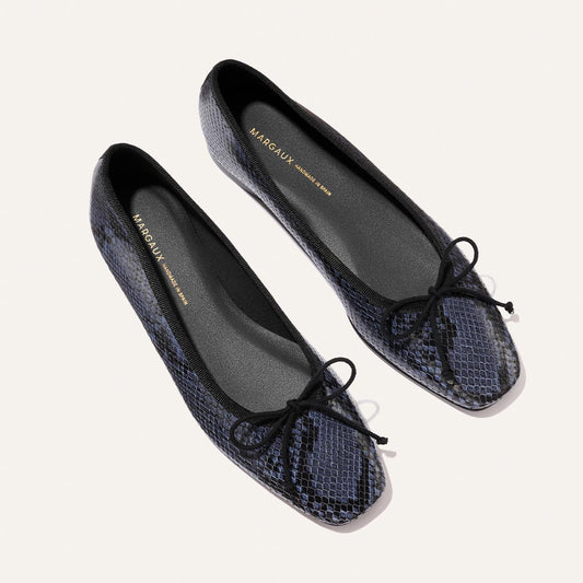 The Fonteyn - Fumo Python Embossed ballet flats by Margaux feature black and navy snakeskin texture, black bows on the toes, and black insoles, displayed against a light background.
