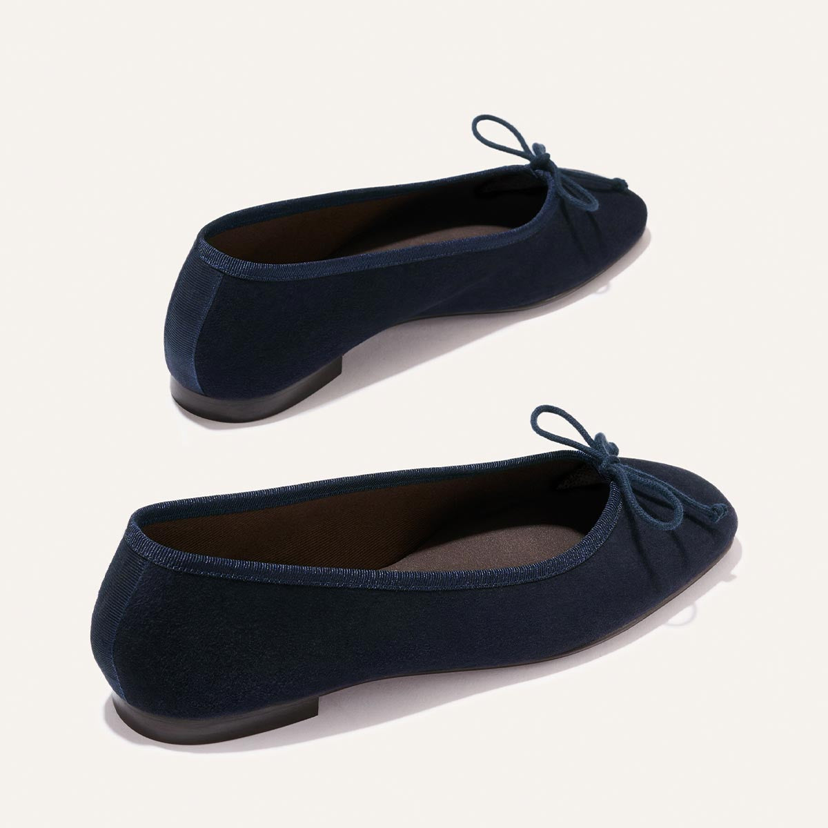 The Fonteyn - Indigo Suede by Margaux: navy blue suede ballet flats with rounded toes and small bows, shown from side and back angles on a plain light background.