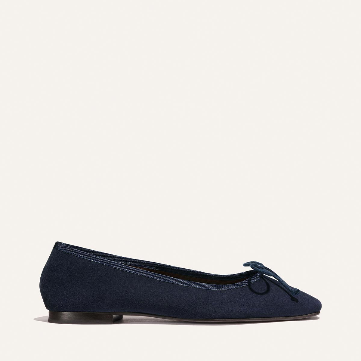 The Fonteyn - Indigo Suede by Margaux is a classic navy blue suede ballet flat with a rounded toe, low heel, and bow detail, shown on a plain white background.