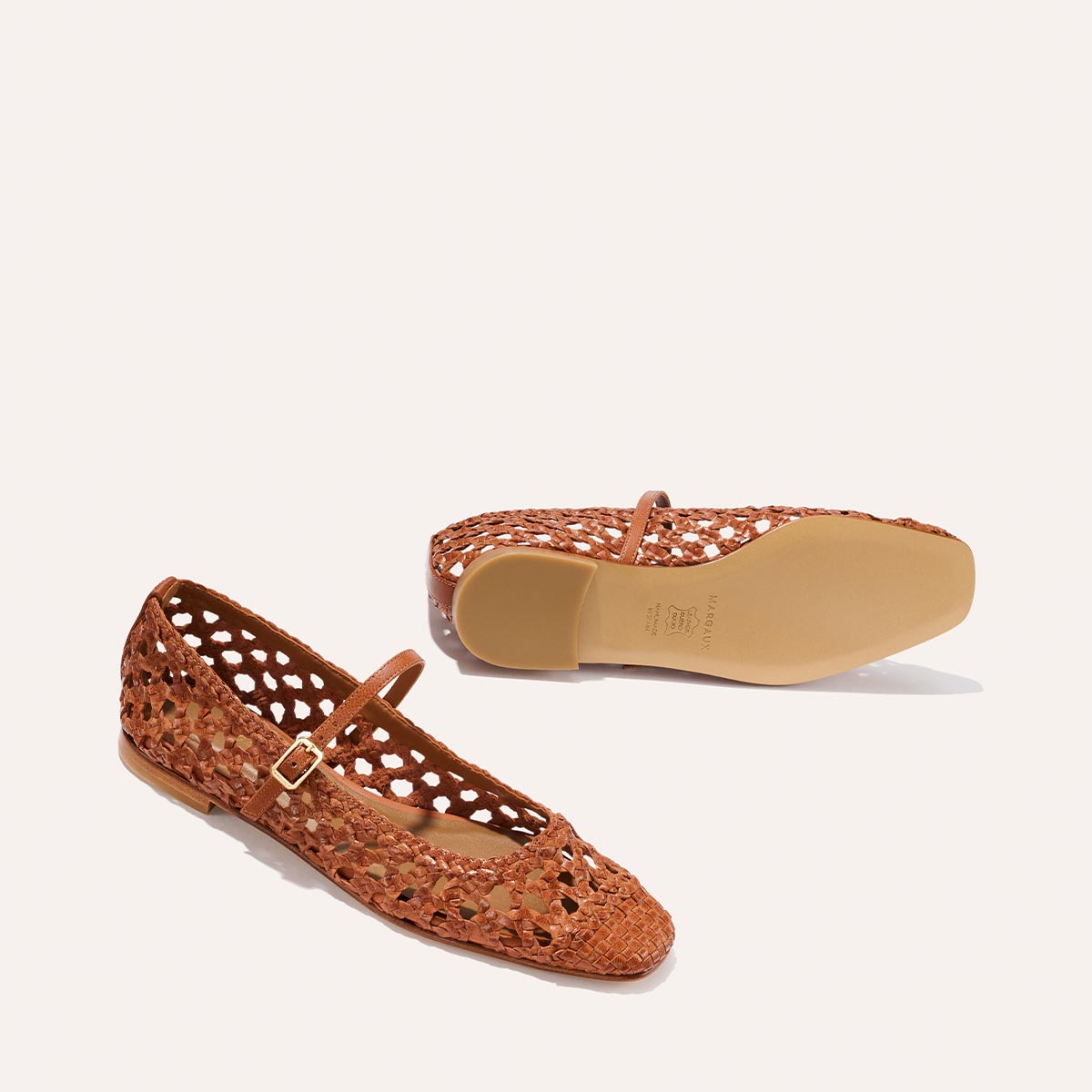 The Margaux Fonteyn Jane flats in Saddle Woven Leather feature a Mary Jane silhouette with buckled adjustable straps and a cut-out design. One shoe stands upright showing side and top views; the other lies flat to reveal the sole.