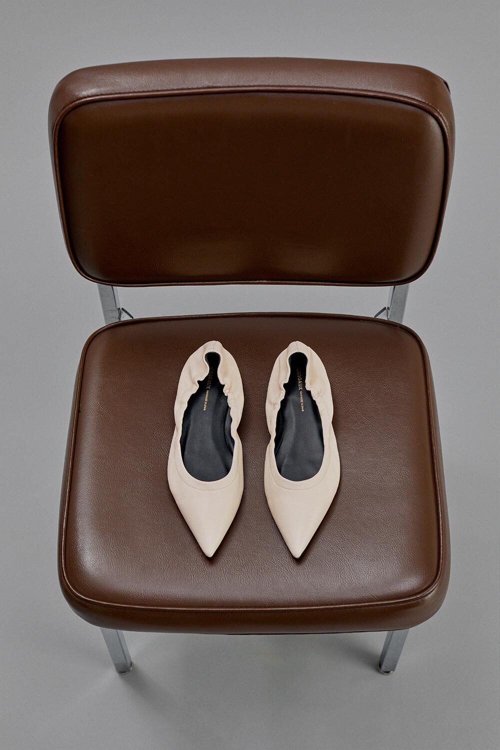 Brown leather shoes on a matching brown chair with a gray background