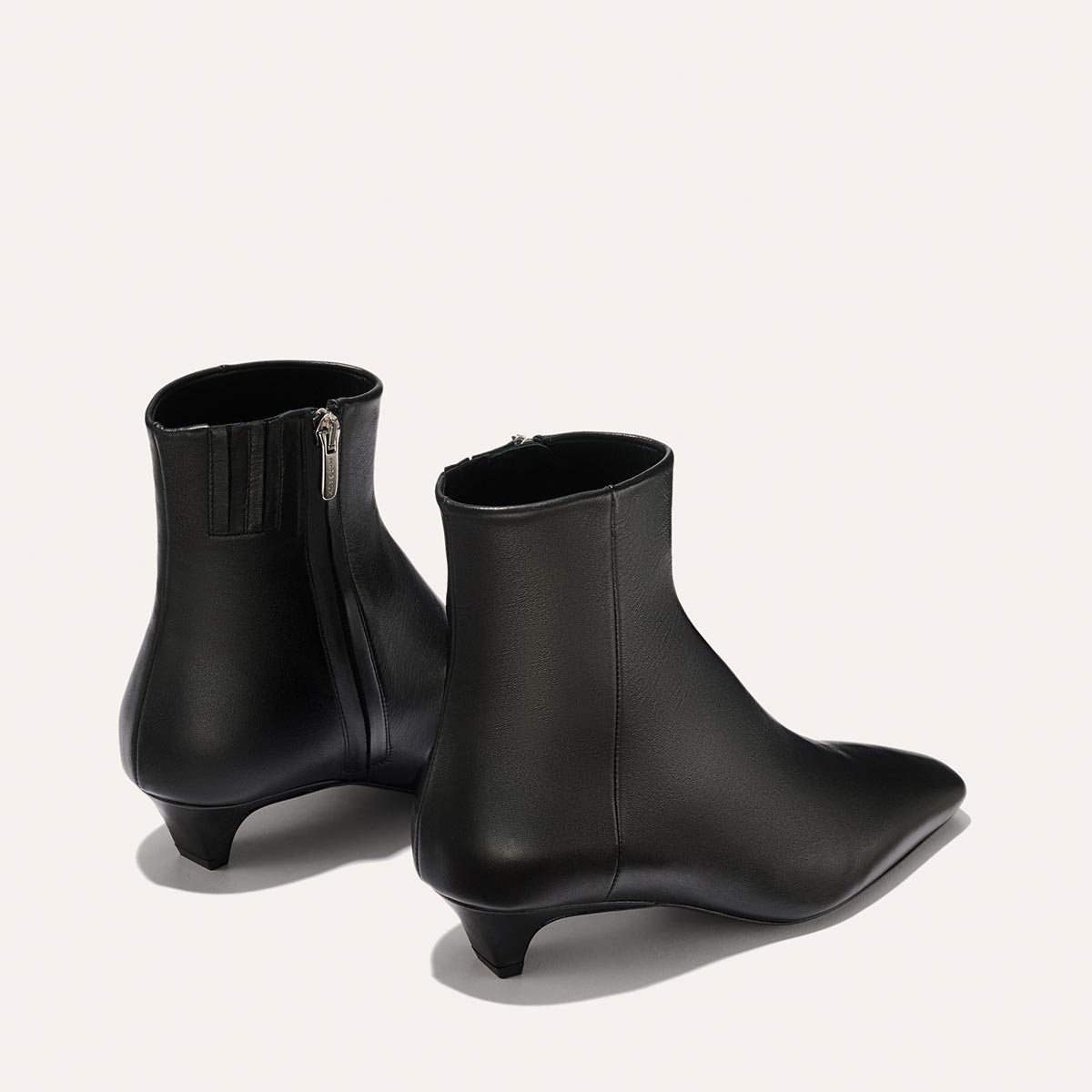 The Inga - Black Calf by margaux-development: sleek black leather ankle boots with pointed toes, low kitten heels, and side zippers—NYC-inspired style shown on a simple light background.