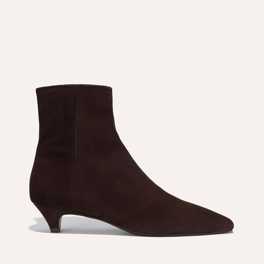 The Inga - Espresso Suede by margaux-development is a dark brown suede ankle boot with a pointed toe and low heel, ideal for city life, shown in profile against a plain light background.