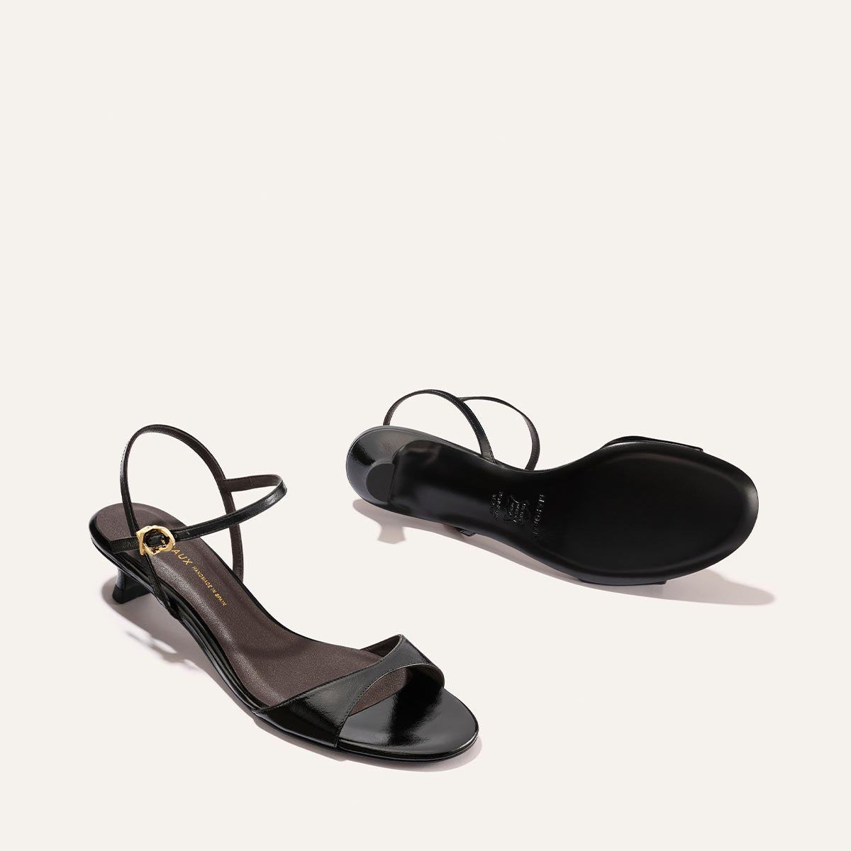 The Lotto 35 by Margaux in Black Crinkle-Gloss Nappa: a pair of heeled sandals with thin ankle straps and low block heels, shown on a neutral background—one upright, one on its side revealing the sole.