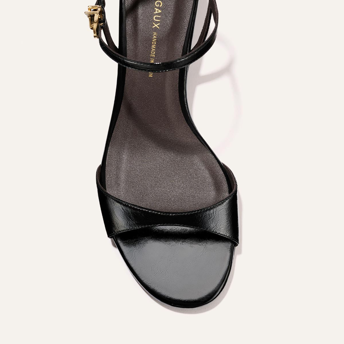 The Lotto 35 - Black Crinkle-Gloss Nappa by Margaux features a black open-toe design with a wide front strap and slim ankle strap with gold buckle, displayed top-down against a light background.