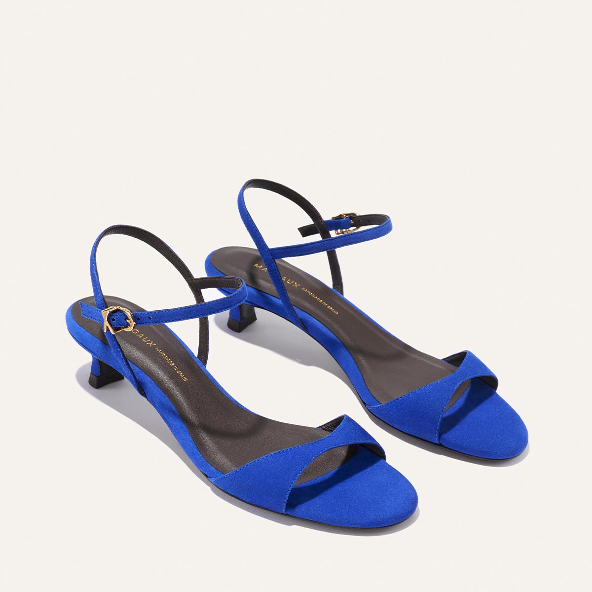 Margaux’s The Lotto 35 - Cobalt Suede sandals feature blue suede, open toes, low kitten heels, and slim ankle straps with gold buckles, shown against a plain white background.