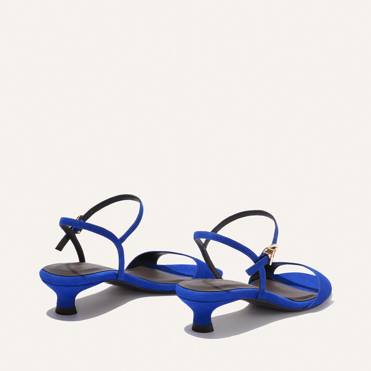 The Lotto 35 - Cobalt Suede by Margaux: blue suede minimal sandals with low kitten heels, black insoles, and thin tapered straps featuring gold ankle buckles, shown on a light background.