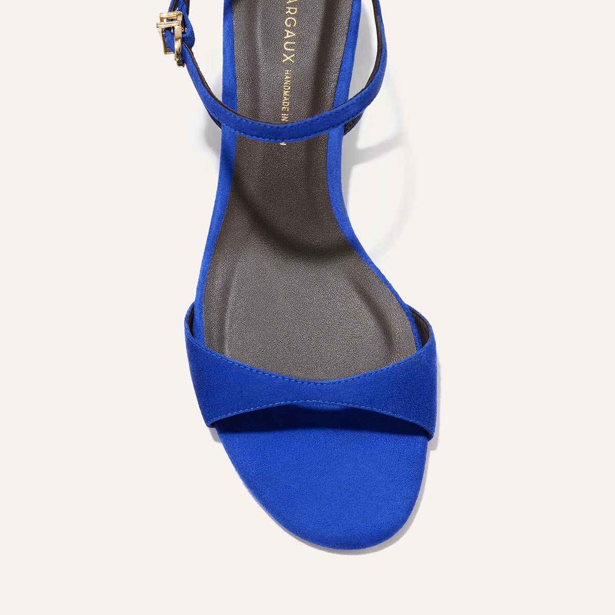 A top view of The Lotto 35 - Cobalt Suede by Margaux, a royal blue minimal sandal with a single tapered front strap and an ankle strap with a gold buckle, displayed on a white background.