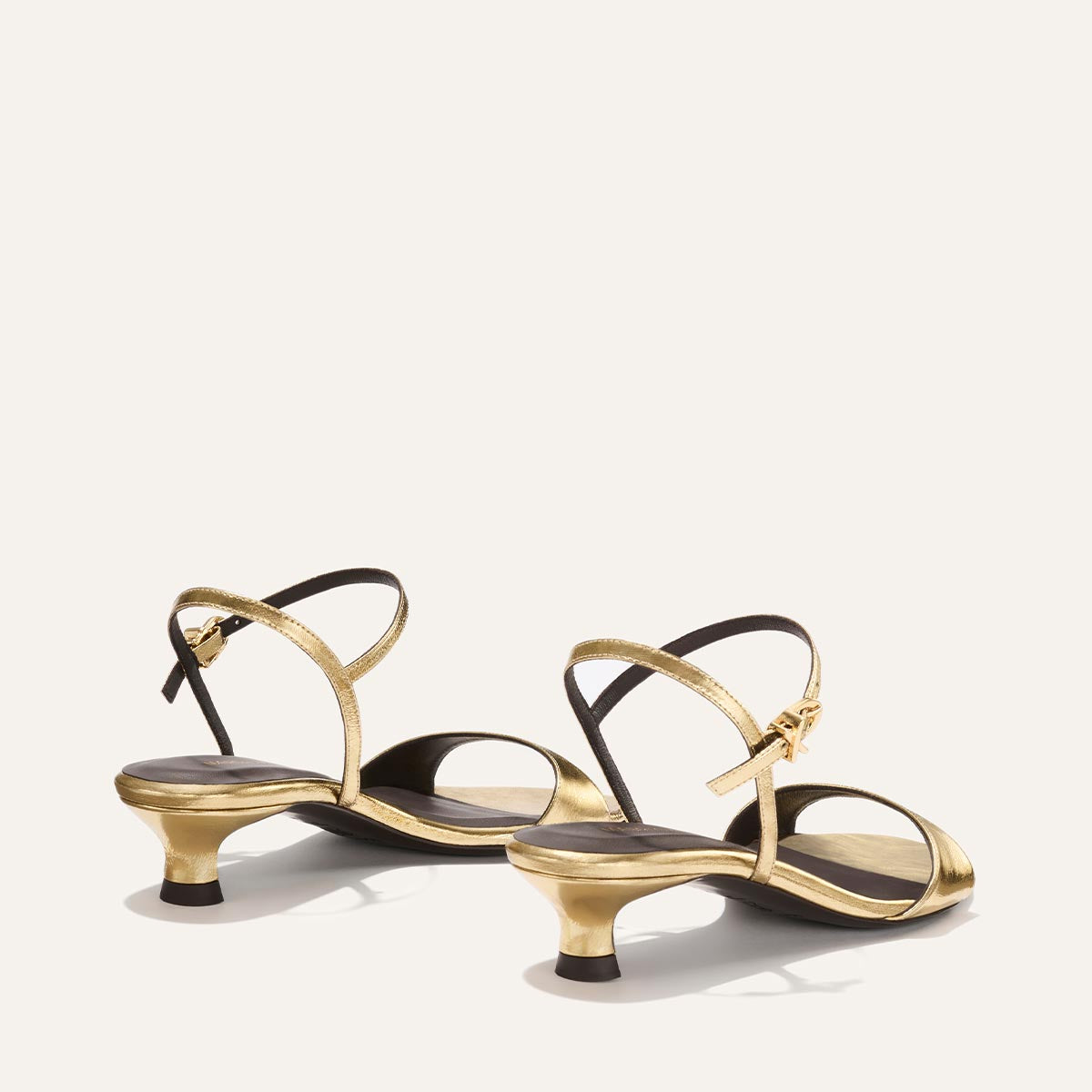 Pair of gold high-heeled sandals with black soles on a white background