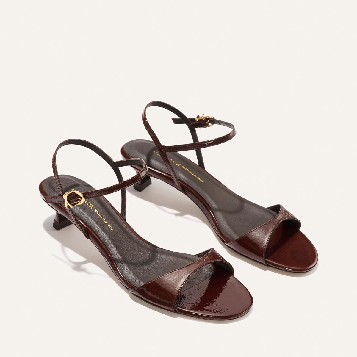 The Lotto 35 - Espresso Crinkle Patent by Margaux: brown strappy open-toe heeled sandals with a low heel and gold-buckled ankle strap, shown on a light background.