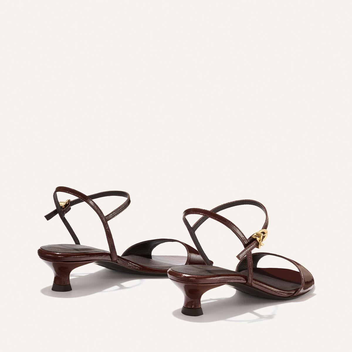 The Lotto 35 - Espresso Crinkle Patent by Margaux: brown strappy low-heeled sandals with gold buckle accents, pictured from an angled rear view on a plain off-white background.