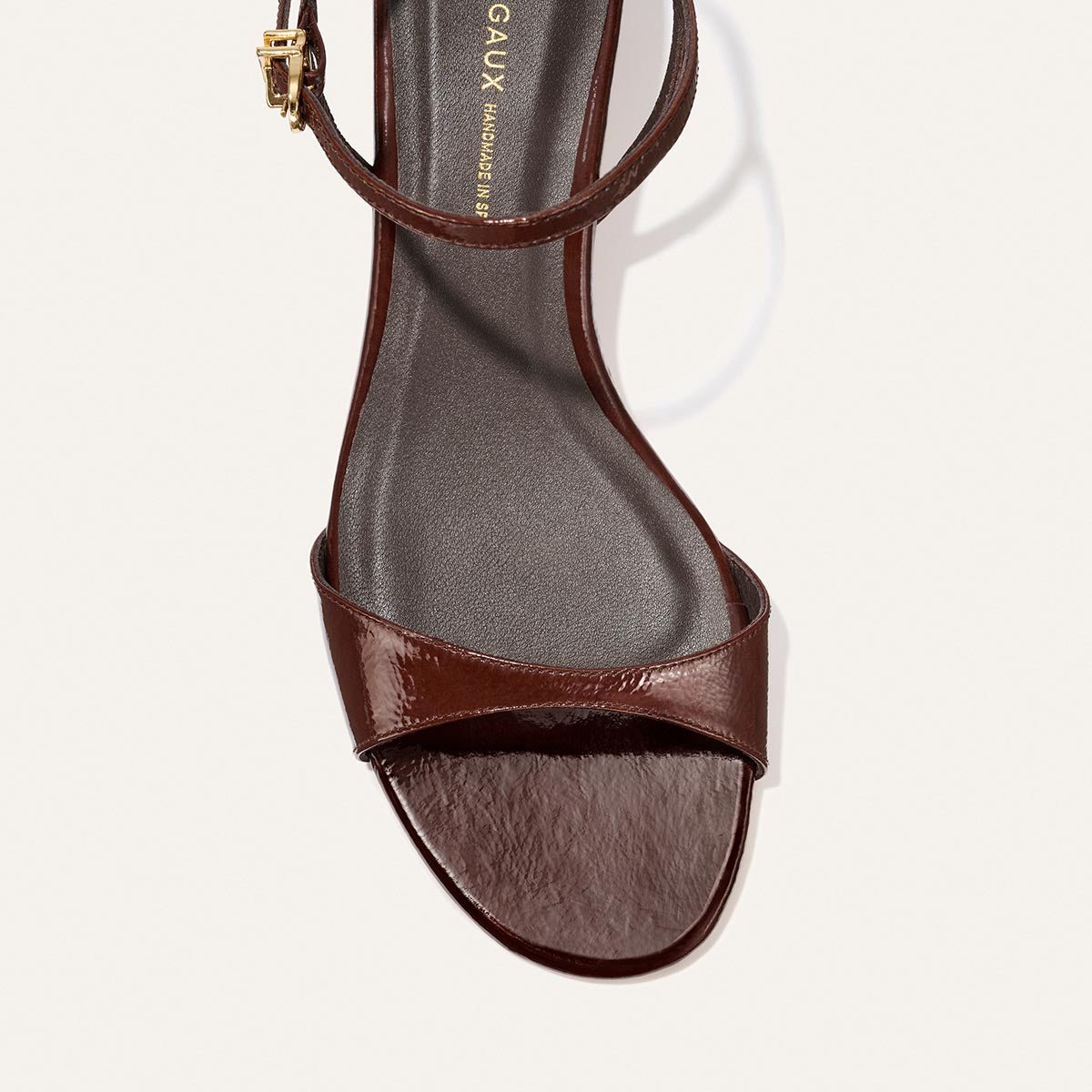 A close-up top view of Margaux's The Lotto 35 - Espresso Crinkle Patent, a brown open-toe heeled sandal with a single toe strap and an ankle strap featuring a small gold buckle.