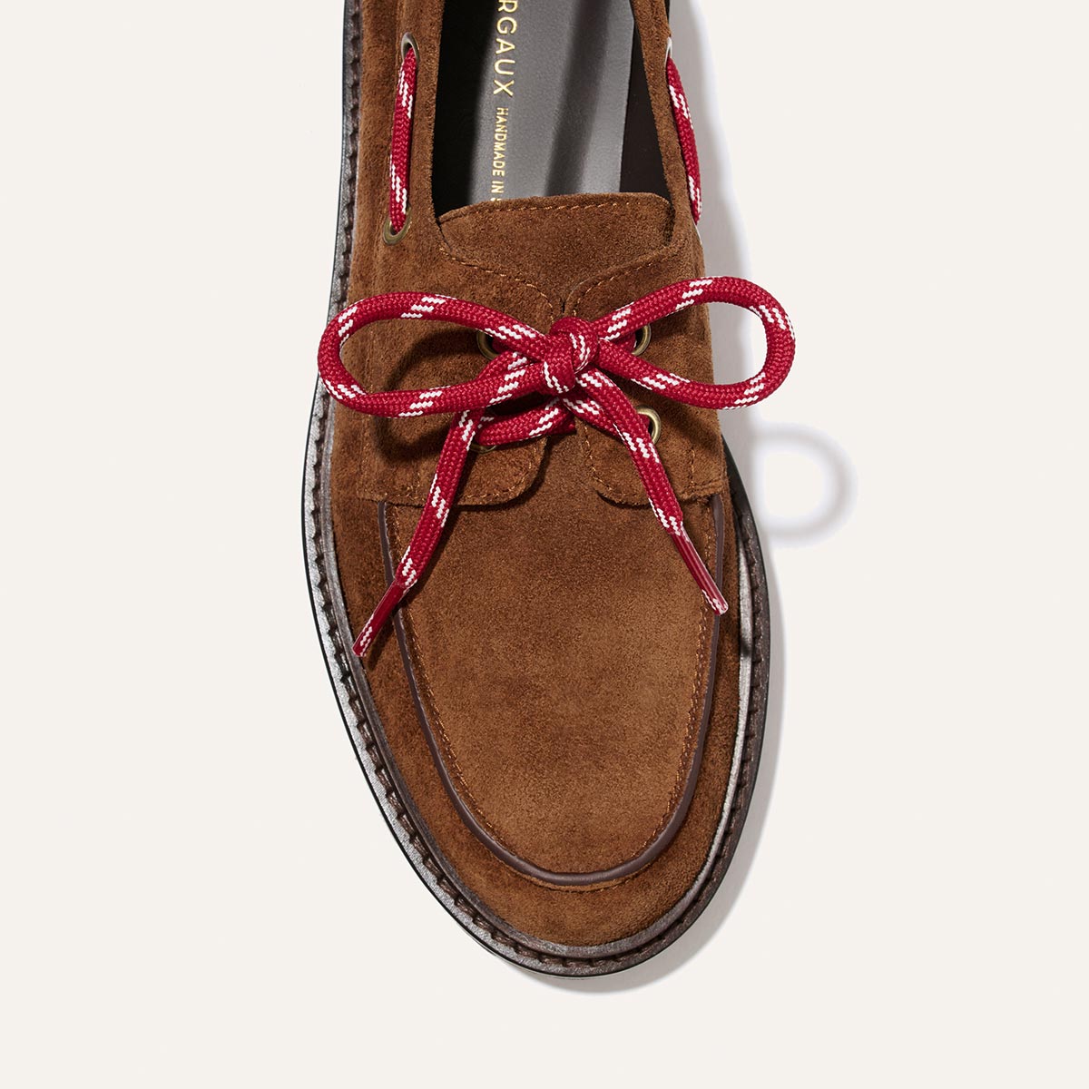 The Marine Loafer - Saddle Suede by Margaux, a brown suede boat shoe featuring a prominent red and white lace tied in a bow, displayed from above against a plain light background.