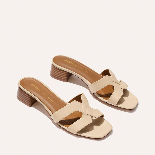 A pair of Margaux’s The MX 35 - Latte Calf heeled sandals, featuring criss-cross straps and mid-height wooden block heels, shown in beige on a light background.
