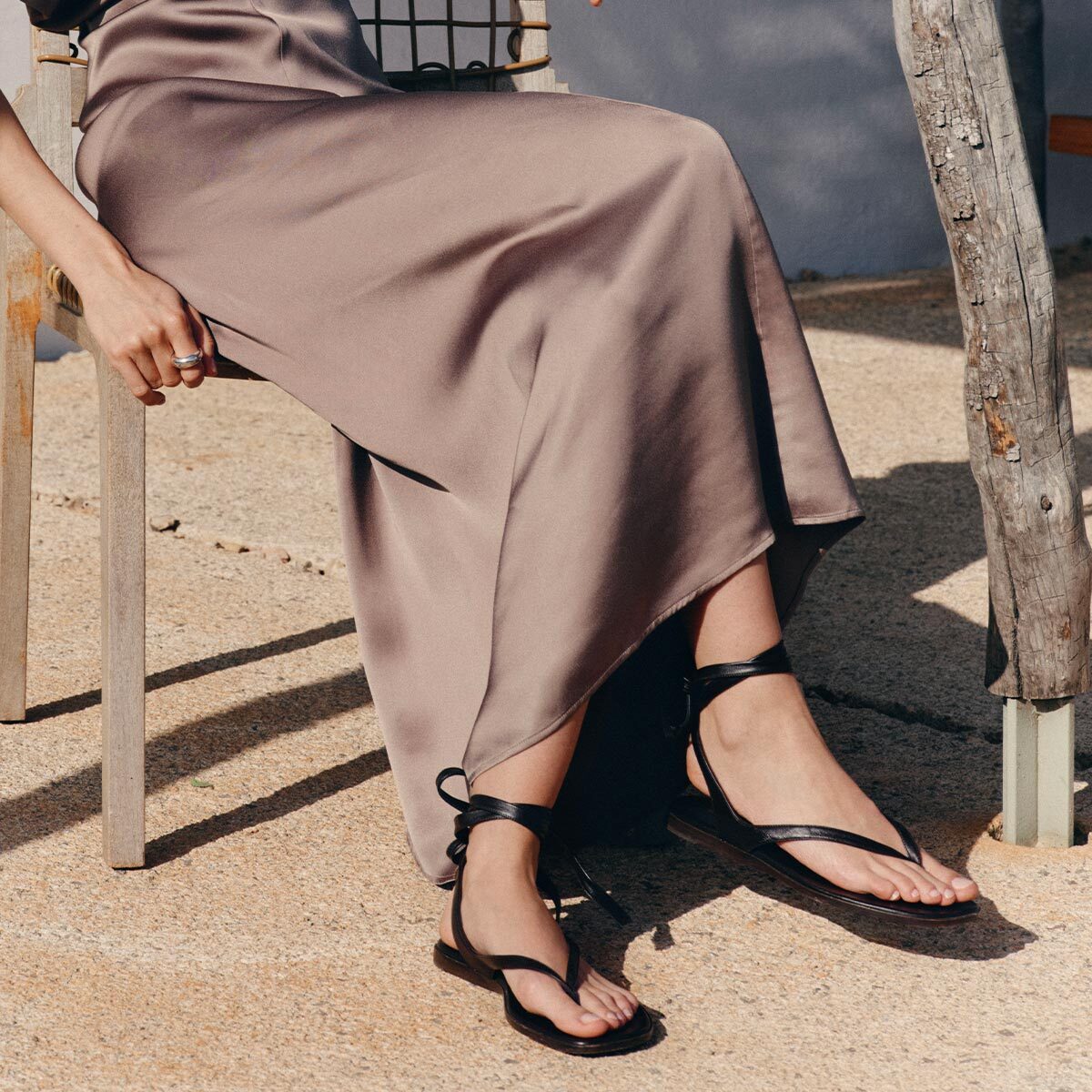 Person wearing a long brown skirt and black sandals sitting outdoors.