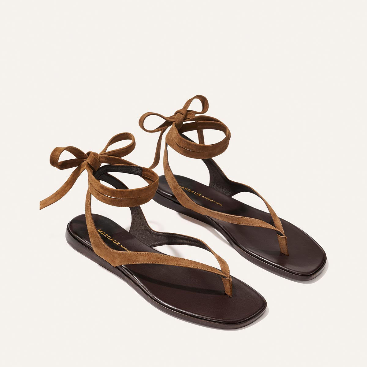 The Palermo Wrap Sandal by Margaux in Nutmeg Suede features minimalistic straps and ankle ties, crafted from suede and displayed on a light background—the perfect flat sandal for summer.