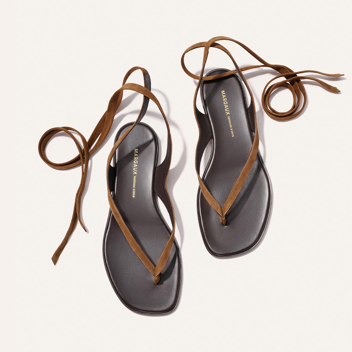 The Margaux Palermo Wrap Sandal in Nutmeg Suede features brown strappy design, long ankle ties, cushioned insoles, and black soles, shown side by side on a light background.