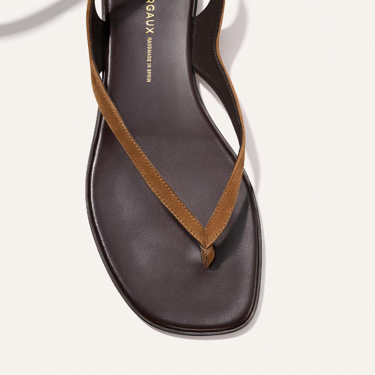 A close-up of Margaux’s The Palermo Wrap Sandal in Nutmeg Suede, featuring a brown square toe, tan suede strap, and cushioned insole—ideal for laid-back getaway style against a white background.