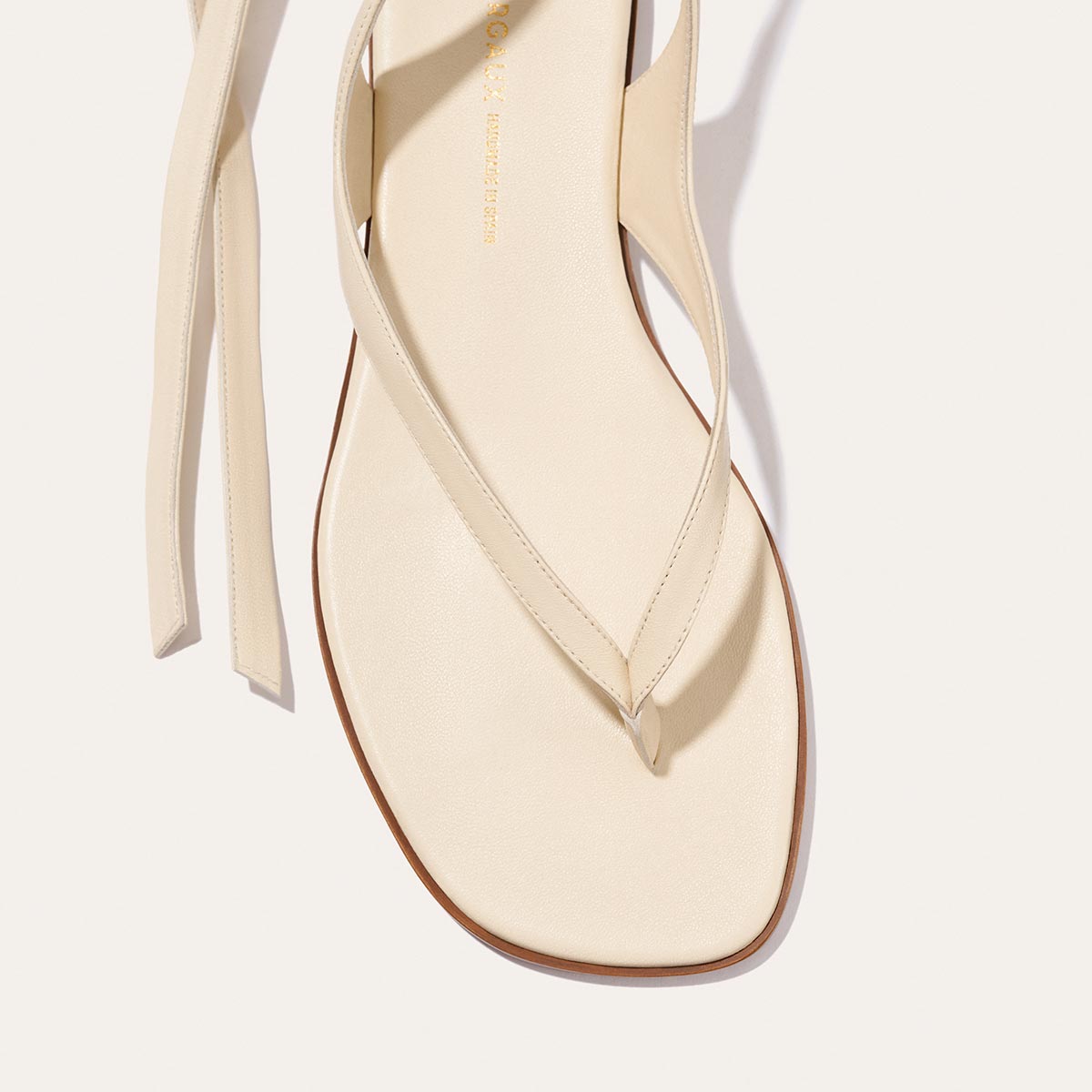 A close-up of Margaux's Palermo Wrap Sandal in Ivoire Nappa, showcasing its minimalistic straps and square toe design, pictured on a light background.