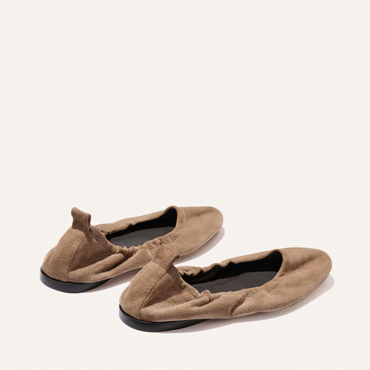 The Pascale - Cappuccino Suede ballet flats by Margaux feature tan suede, elasticated backs, and black soles, shown side by side on a plain light background.