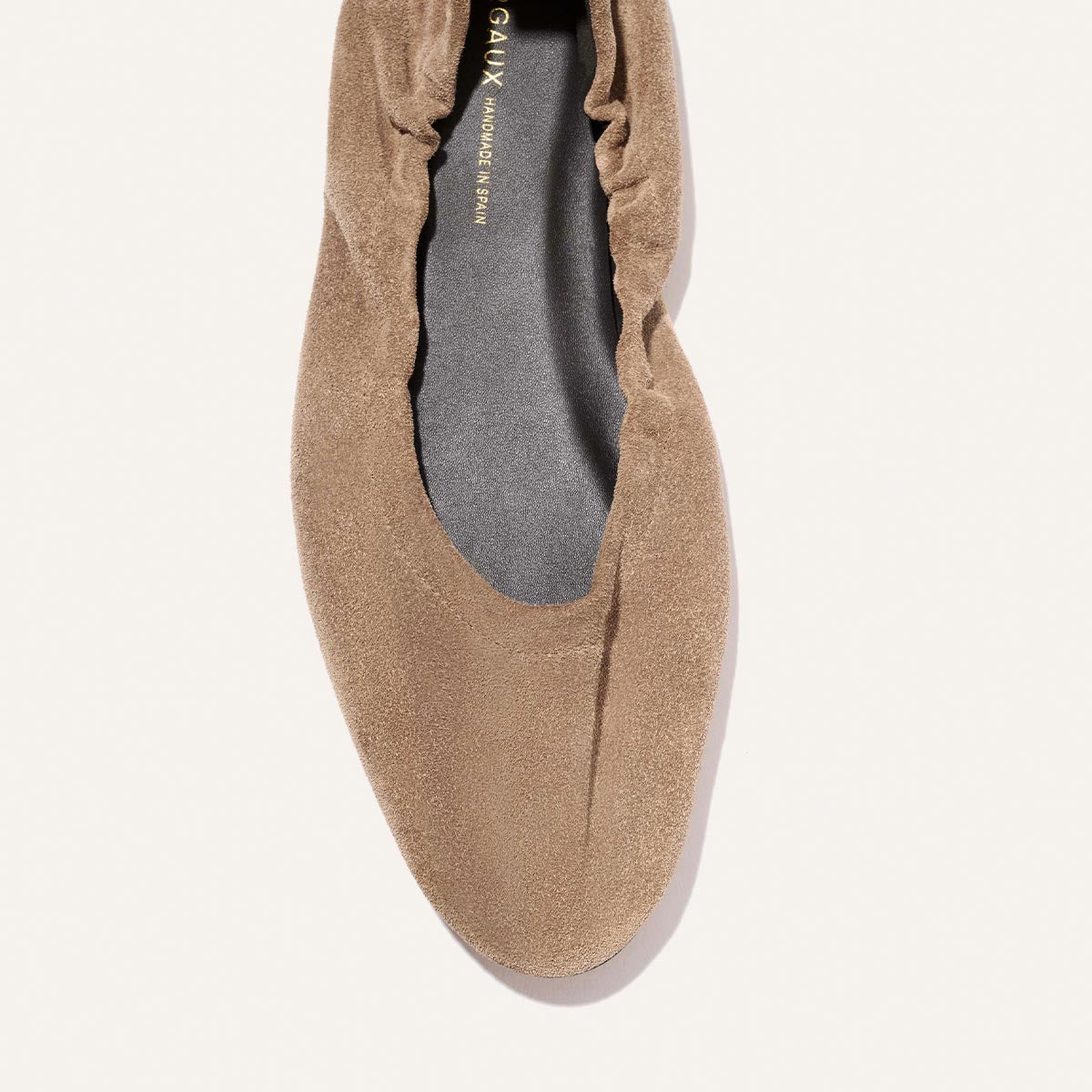 A close-up top view of Margaux’s The Pascale - Cappuccino Suede ballet flat showcases its elasticated back, ruched heel, and dark insole, photographed on a light background.