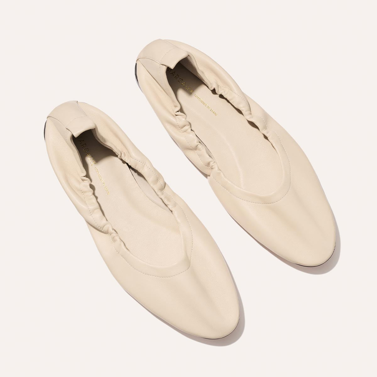 The Pascale - Bone Nappa by Margaux: cream-colored women's ballet flats with gathered elastic sides, shown from above on a light background.