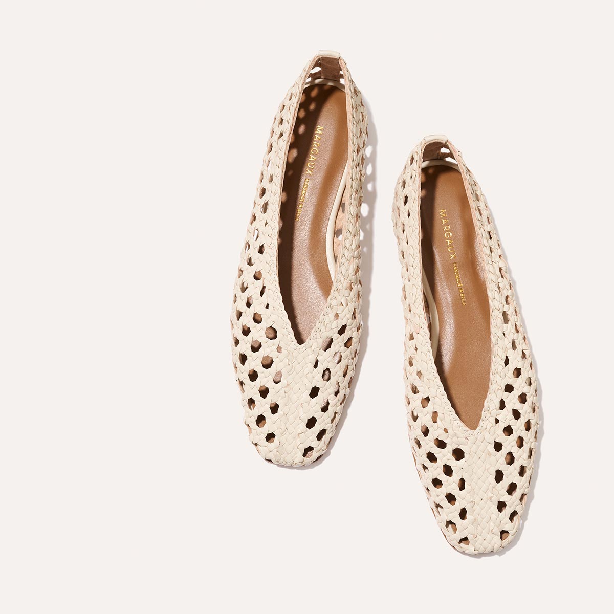 The Margaux Woven Paz SS25 in ecru leather are cream-colored flats with a handwoven, perforated design, pointed toes, and tan insoles featuring gold Paz text, shown against a plain white background.