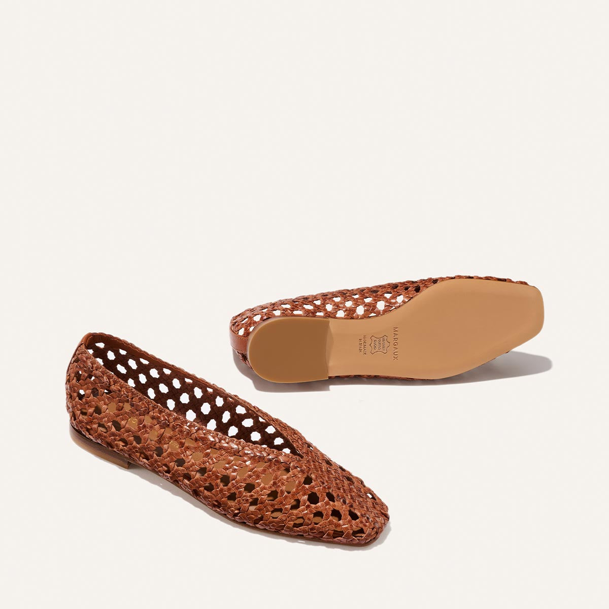 Two Margaux "The Woven Paz - Saddle Woven Leather" flats are displayed on a white background—one upright, the other sole-up revealing the brand. They feature a pointed toe, higher rise, and handwoven open weave design.