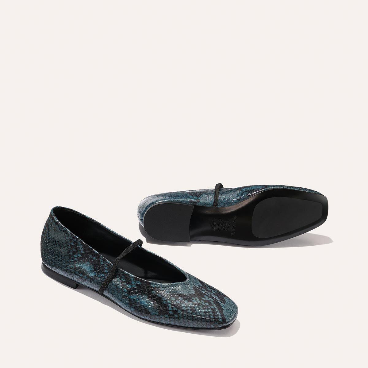 The Phoebe - Aqua Python Embossed by Margaux: flat Mary Jane shoes with blue and black snakeskin pattern and black elastic straps, shown from side and bottom views against a light background.