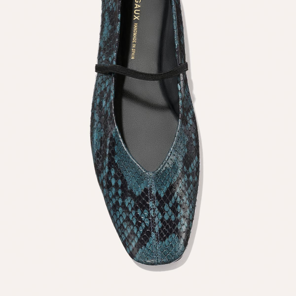 A close-up top view of The Phoebe - Aqua Python Embossed flat shoe by Margaux, featuring teal and black python-textured leather, a square toe, and a thin black front strap.