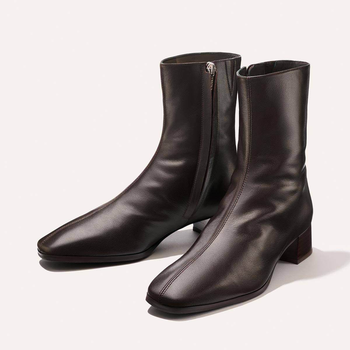 A pair of Margaux’s The Phoebe Boot in Dark Chocolate Calf, featuring side zippers, square toes, and low stacked leather heels, displayed on a light background.