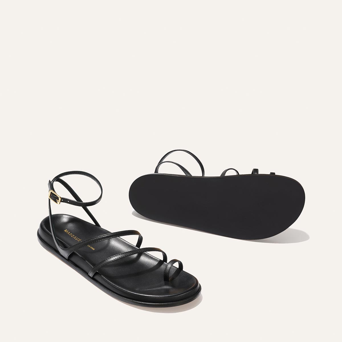 Black sandal with thin straps on a light beige background